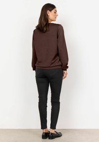 Sudadera marrón de manga larga, con cuello redondo y corte relajado. Combinada con pantalones ajustados negros y mocasines negros. Fondo liso.