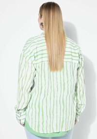 Camicia a maniche lunghe con motivi a righe bianche e verde chiaro, vestibilità rilassata, polsini abbottonati, dettaglio con yoke sul retro e orlo arrotondato.