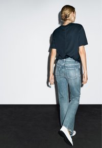 Un t-shirt noir à manches courtes associé à un jean droit bleu clair. Le jean possède des poches arrière avec des coutures contrastées et une finition délavée.