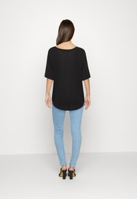 Maglietta nera oversize con scollo a barca, abbinata a jeans skinny blu chiaro e sandali neri con tacco a blocco, vista da dietro.