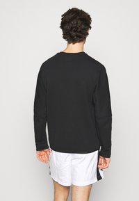 Musta pitkähihaisen collegepaita, jossa on sileä pinta ja yksinkertainen muotoilu, pyöreä pääntie ja suora helma, päällä valkoiset shortsit.