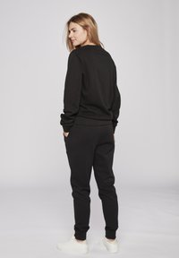 Zwarte sweatshirt en broekset gemaakt van een zachte katoenmix. De outfit heeft een relaxte pasvorm, ribgebreide manchetten en zichtbare zakken.