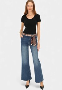 Czarny dopasowany top z krótkim rękawem zestawiony z dżinsami o wysokim stanie i szerokich nogawkach, ozdobionymi brązowym paskiem z wzorem. Stylizację uzupełniają czarne szpilki.