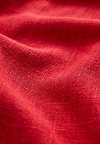 Roter Leinenstoff mit einer strukturierten, leicht zerknitterten Oberfläche, die ein weiches, natürliches Gewebe und eine satte Farbe zeigt.