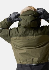Groene waterdichte jas met een met bont gevoerde capuchon, voorzien van een zwarte ondersectie, geborduurd logo en gestructureerde grijze handschoenen.