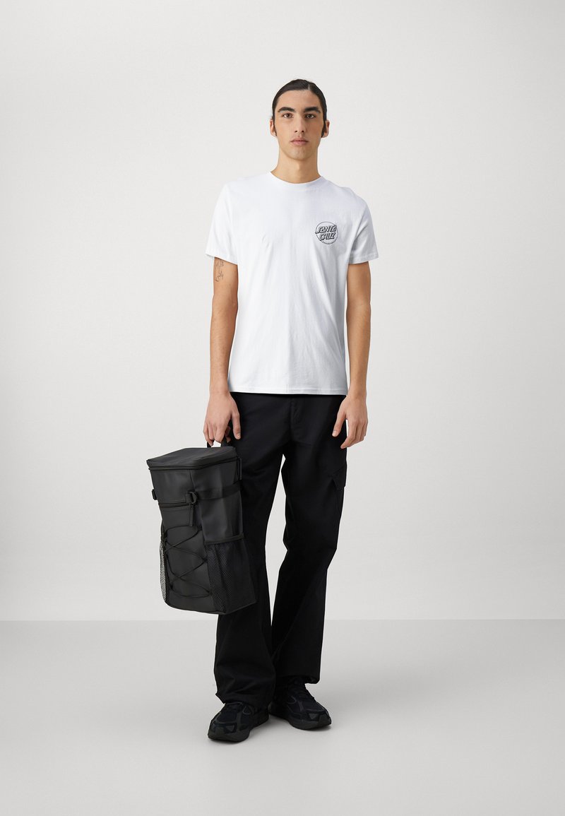 Vit bomull t-shirt med en liten svart grafik, kombinerad med svarta cargo-byxor och en svart cylindrisk ryggsäck med nätliknande detaljer.