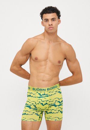 Sárga férfi boxeralsó zöld absztrakt hullámmintával, zöld derékpánttal, amelyen a "BJÖRN BORG" felirat olvasható. Anyaga lágy és rugalmasnak tűnik.