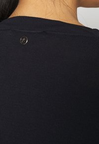 Mörkblå stickad tröja med rundad halsringning, med en liten guldig logotypdetalj på baksidan, strukturerad med fina ribbor hela vägen.