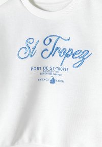 Felpa bianca con testo ricamato blu che recita "St Tropez", disegni di un veliero e le frasi "PORT DE ST-TROPEZ" e "FRENCH MARINA."