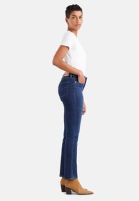 Denim jeans in dark blue, straight leg design. Worn with a fitted white t-shirt and brown heeled ankle boots, featuring signature back pockets.
