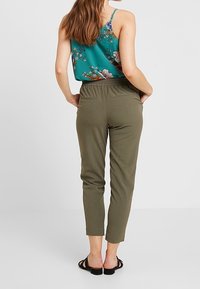Débardeur floral vert à fines bretelles, associé à un pantalon olive taper. Le pantalon a une taille élastique et des poches obliques.