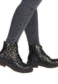 Bottines à lacets en imprimé léopard noir et doré, avec fermeture éclair sur le côté, en cuir texturé et semelles en caoutchouc épaisses, assorties à un jean skinny gris.