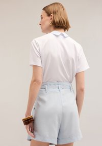 Tricou alb cu mânecă scurtă, având guler în dungi albastre, asociat cu pantaloni scurți galben deschis, cu talie lată și buzunare laterale.