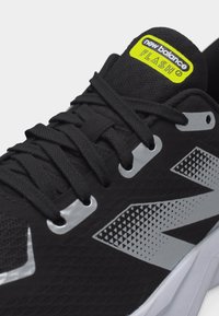 Μαύρο παπούτσι για τρέξιμο New Balance με γκρι λογότυπο και αντανακλαστικές τρύπες για τα κορδόνια, με ετικέτα «Flash» στη γλώσσα και χοντρή λευκή σόλα.