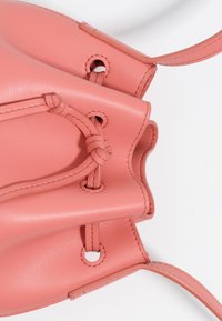 Różowa skórzana torba typu bucket z teksturowaną powierzchnią, z sznurkiem do ściągania i metalowymi oczkami, a także węzłowymi akcentami na ramiączkach.