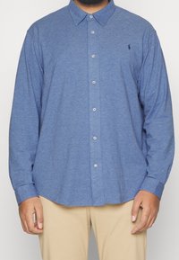 Niebieska koszula zapinana na guziki, wykonana z teksturowanej tkaniny, z klasycznym kołnierzykiem i długimi rękawami, z małym logo na lewej piersi.