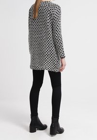 Lång svart och vit mönstrad tröja med avslappnad passform, parat med svarta leggings och ankelskor. Slät tygtextur, minimalistisk design.