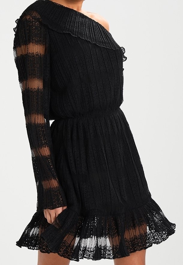Robe en dentelle noire avec une manche épaule dénudée, texture côtelée, manche longue rayée transparente et ourlet à volants portée par un mannequin.