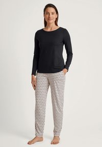 Zwarte lange mouwen top gecombineerd met een patroonloze, losse broek in crème met een herhalend ontwerp. De stof lijkt zacht en ademend.