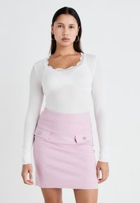 Valge pika varrukaga topp pitsist kaelusega, millele on sobitatud roosa tekstuuriga mini-seelik, millel on kaks esist taskut ja ümmargused detailid.