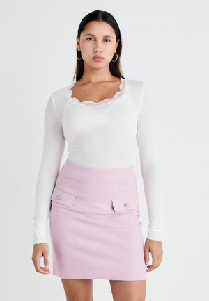 White long-sleeve top with lace neckline paired with a pink textured mini skirt featuring two front pockets and round hardware accents.