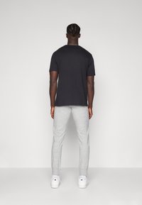 Zwarte katoenen T-shirt en lichtgrijze sweatpants; T-shirt heeft een ronde hals, en de broek heeft elastische boorden; gecombineerd met witte sneakers.