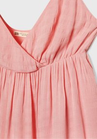 Robe de couleur pêche avec un col en V, tissu texturé et taille froncée. Présente des motifs subtils et une drapé fluide et lisse.