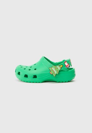 Green clog made of synthetic material, featuring ventilation holes, a rounded toe, and decorative charms depicting a Christmas tree and Santa.