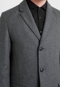 Grijze wollen blazer met een gladde textuur, voorzien van een notched lapel, drie zwarte knopen en een getailleerde pasvorm, gecombineerd met een zwart shirt.