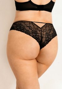 Czarny koronkowy thong z kwiatowym wzorem, z niskim stanem i minimalnym kryciem. Miękka faktura z cienkimi ramiączkami i falistymi krawędziami.