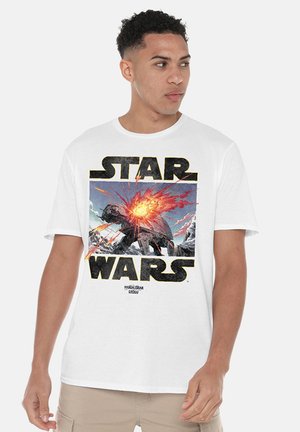 Man wearing white Star Wars t-shirt with large graphic of an exploding AT-AT walker from The Mandalorian series.