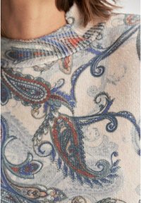 Strickpullover aus einem weichen, strukturierten Stoff mit einem hellbeigen Hintergrund und komplizierten blau- und rotfarbenen Paisleymustern am Kragen.
