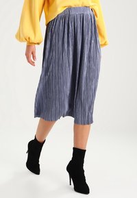 Gonna midi plissettata blu con vita elastica, caratterizzata da morbide righe verticali, abbinata a stivaletti neri con tacco.