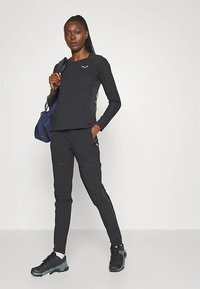 Černý sportovní top a kalhoty z hladké pružné látky. Top má kulatý výstřih a nenápadné logo; kalhoty mají kapsy na zip. Obuv je černá s texturovanými akcenty.