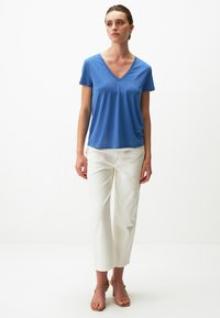 Niebieska, krótko rękawowa koszulka V-neck w luźnym kroju, zestawiona z białymi spodniami o prostym kroju i beżowymi sandałami na obcasie z paskami.