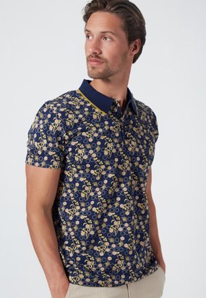 Polo de manga corta en azul oscuro con un patrón floral y hexagonal en amarillo y beige. Presenta un cuello y tapeta de botones en contraste en color marino.