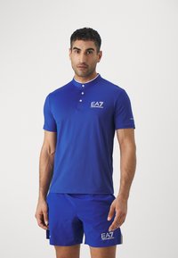 Mėlyna trumpomis rankovėmis polo marškinėliai su apykakle, trimis mygtukais priekyje ir EA7 logotipu ant krūtinės. Lygus, atletinis siluetas.