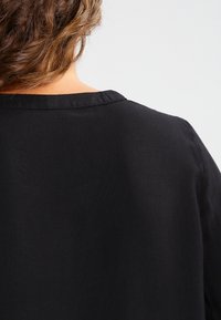Top in tessuto nero leggero con scollatura rotonda semplice e maniche corte, che mostra la trama e i dettagli di costruzione nella parte posteriore.