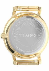 Kuldtooni randmepulk roostevabast terasest tagaküljega, hall nägu, millel on "TIMEX" logo ja poleeritud äär. Klassikaline disain, millel on minimaalsed detailid.