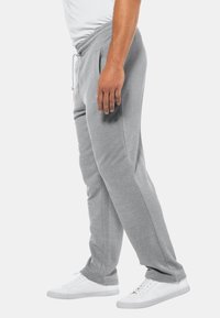 Grå joggingbukser med snoreliv, sidelommer og tapered fit, parret med hvide sneakers på en neutral baggrund.