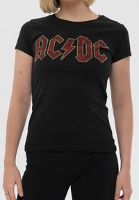 Black cotton t-shirt featuring red and gold studded AC/DC logo, short sleeves, and a fitted shape, suitable for casual wear.