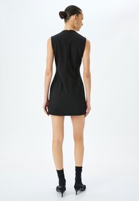 Abito mini senza maniche di colore nero con un design aderente, cerniera sul retro senza cuciture e tessuto liscio. Abbinato a calzini neri e scarpe con tacco alto.