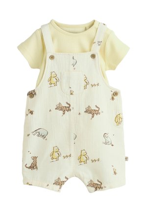 T-shirt bébé jaune à manches courtes côtelé sous une salopette crème avec bretelles à boutons avec des motifs d’ours, tigre, lapin et caneton dessin animé.