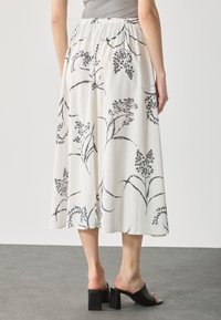 Vit midikjol med svart blommönster, elastisk midja, svängig tyg och en smidig textur; matchad med svarta klackskor i block.