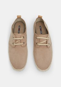 Perforated beige lace-up shoes with a tan textile upper, round toe, and a natural fiber sole. Features a logo tag on the inside.