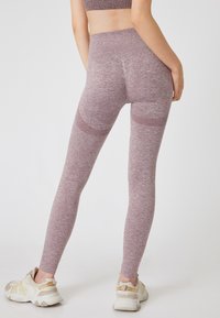 Mauve legging met een gestructureerd, gemêleerd patroon, hoge tailleband en een aansluitende snit, gecombineerd met lichtgekleurde sportschoenen.