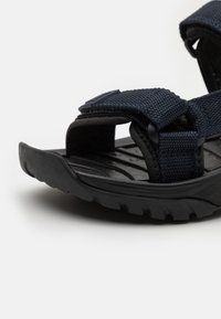 Mustat sandaalit, joissa on nylonstrappit, teksturoitu pohja, avoin kärki ja säädettävät velcro-kiinnitykset, sopivat ulkokäyttöön.