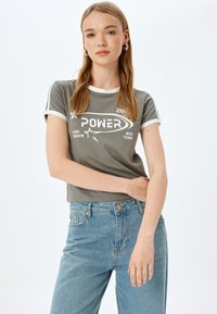 Grijze cropped t-shirt met witte accenten, met een grafische print waarop het woord "POWER" staat, gecombineerd met blauwe high-waisted jeans.