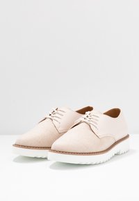 Scarpe beige stringate con una tomaia in tessuto testurizzato e accenti in pelle liscia. Caratterizzate da una suola bianca scanalata e cuciture a contrasto lungo il bordo.