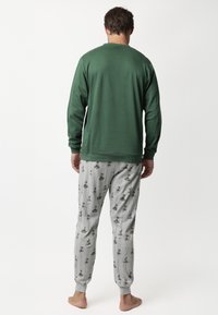 Camiseta de manga larga verde con cuello acanalado, combinada con pantalones de pijama grises que presentan un patrón gráfico repetido de pequeños objetos y acentos.